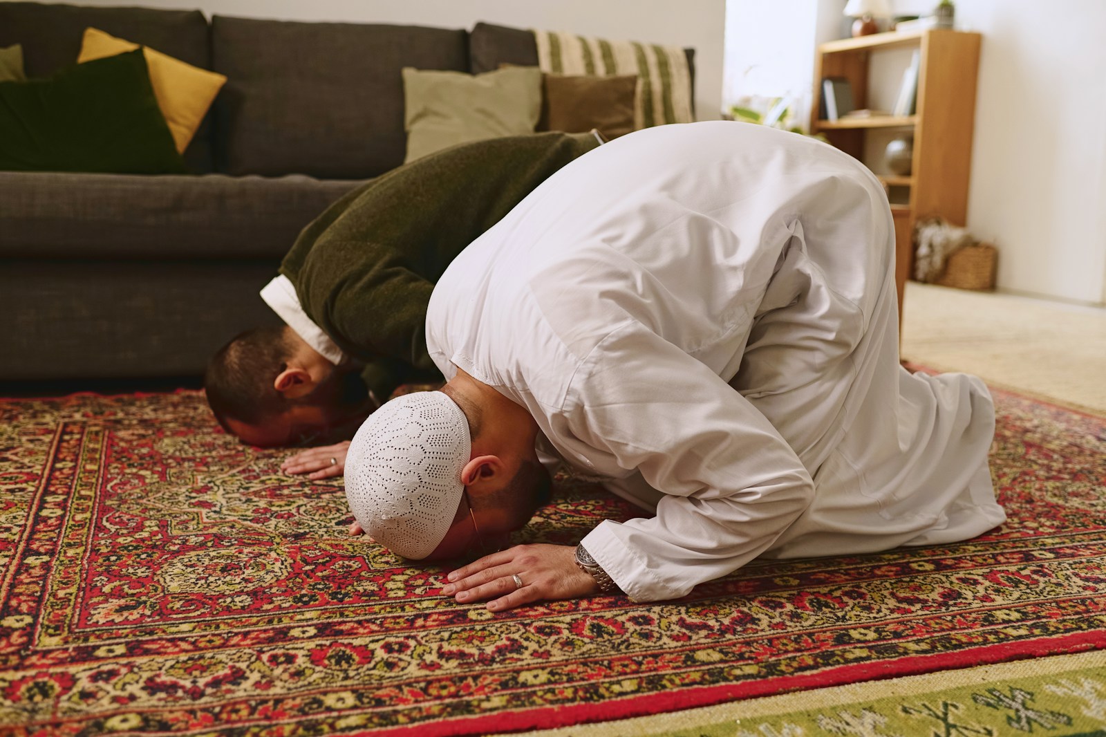 a man in a white outfit is praying on a rug